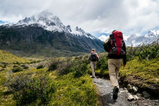 Zwei Personen wandern in Richtung schneebedeckter Berge in Chile.