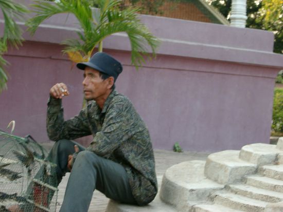 Vogelhändler beim Rauchen vor einem Tempel in Phnom Phen: Der Käufer lässt den Vogel meist sofort frei, um Pluspunkte fürs nächste Leben zu sammeln.
