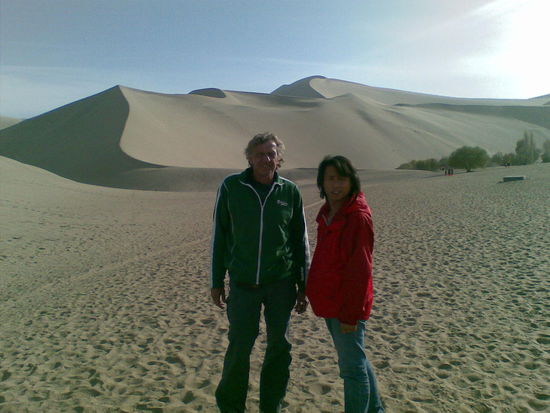 Touri-Foto Nr. 1: Urs mit Tony vor den Mingsha Bergen.
Rutscht man den Gipfel herunter, so gibt der Sand Töne von sich, was auch der Ursprung des Namens besagt. ("Mingsha" bedeutet in der chinesischen Sprache "erklingender Sand").
Historischen Aufzeichnungen zufolge war der Schall wie ein Ensemblesstück auf traditionellen chinesischen Musikinstrumenten von diesem Berg aus zu hören.