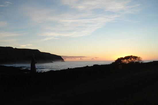 Sonnenaufgang an der Kueste mit einem Moai im Vordergrund.