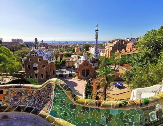 Ausblick vom Park Güell über Barcelona mit den berühmten Mosaiken und den markanten Gebäuden von Antoni Gaudí im Vordergrund.