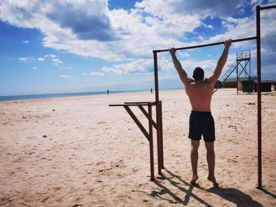 Mann trainiert mit Klimmzügen an einer Stange am Strand
