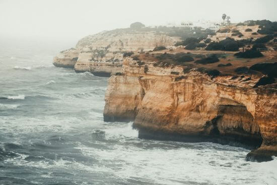 Blick auf die steilen Felsen und das raue Meer an der Algarve-Küste in Portugal an einem nebligen Herbsttag.