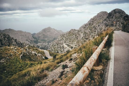 Kurvige Bergstraße mit Holzgeländer in der Serra de Tramuntana auf Mallorca an einem klaren Herbsttag.