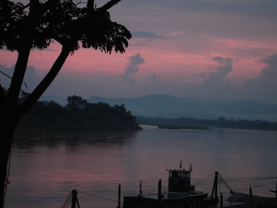 Sonnenaufgang in Chiang Kong. Zur rechten Zeit am richtigen Ort.
Da bin ich wieder, im Guesthouse mit Internet Anschluss. 
Am Montag Morgen bin ich wieder vor dem Wecker erwacht, da ich auf jedenfall eine der Ersten beim Zollhaus sein wollte. Darum hatte ich noch genügend Zeit, mich am Ufer des Mekong umzuschauen. Der Tag war gerade so am erwachen und ich drückte auf den Auslöser meiner Fotokamera. Daraufhin ist dieses Bild entstanden. 
Die Wirtin war so nett und ist extra wegen mir sooo früh aufgestanden, hat mir einen Tee zubereitet und ich habe ihr mit meinen Händen gezeigt, dass ich gerne 2 Toastbrote mit Butter und Konfi wünsche. Als ich es ihr bezahlen wollte, hatte sie es abgelehnt, darum gab ich ihr noch ein schönes Trinkgeld. Dann hielt sie für mich an der Strasse noch einen Tuk-tuk-Fahrer an, der mich mit meinem schweren Koffer zum Pier bringen sollte. Fünf Minuten später war ich am Zoll und stellte mich zu den dort bereits wartenden Touristen. Punkt 8.00 öffnete der Zöllner sein Fenster und wir konnten unsere Pässe zur Ausreise vorzeigen.