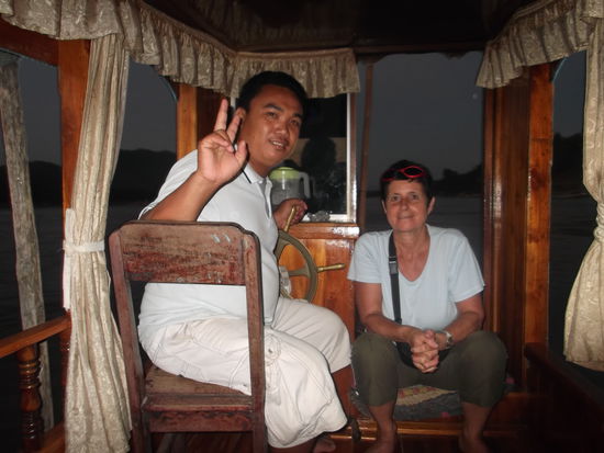 Unser Kapitän "Sam Ok"
Als ich so gegen 17.00 Uhr am Namkong vorbei spazierte, fragte mich ein Laote, ob ich mit ihm eine Sonnuntergangsfahrt machen möchte. Ich fragte nach dem Preis und er erwiedert, für 150'000 Kip. Als ich ihm sagte, ich möchte gerne meine Freundin mitnehmen, kam er mir sogar noch bis auf 120'000 Kip entgegen. Für diesen Preis kann man wirklich nicht mehr viel sagen. Es war ein herrlicher Abend und eigentlich hatte ich schon Lust dazu, wollte aber gerne mit Uta diese Tour unternehmen. Als ich im Guesthouse ankam, fragte ich sie nach ihrem Programm. Sie war damit einverstanden, und so begaben wir uns wieder ans Ufer des Mekong. Es war wirklich der schönste Abend dieser Woche, das seht ihr ja im Foto. Er nahm uns mit auf ein Slowboot, wo ca. 25 Personen darauf Platz gefunden hätten. Als ich so mit ihm plauderte, erzählte er, dass er schon seit 12 Jahren das Boot seines Vaters steure. Aber es hätte zu viele Boote in Luang Prabang und so gäbe es manchmal Tage, da er gar keine Fahrt unternehmen kann. Darum ist er uns auch so sehr entgegen gekommen. Som Ok ist 37 und hat eine noch sehr junge Frau. Sie ist 25 und sein ältestes Kind ist bereits 11 Jahre alt. Dann hat er noch einen Nachzügler mit 4 Jahren. Das ist für ihn sicher nicht sehr einfach, wenn er Geld verdienen sollte und er dann 1 oder 2 Fahrten den ganzen Tag machen kann. Ich habe ihn gefragt, ob er denn Visitenkarten an seine Gäste abgebe. Aber davon hat er keine Ahnung. Ich habe ihm versprochen, welche am PC zu schreiben, und ihm diese dann auf perforiertem Papier ausgedruck zu senden. Wir haben wieder frisch und fröhlich thai, lao und englisch durcheinander gesprochen. Er meinte, woher ich denn so gut laotisch sprechen gelernt habe. Da musste ich nur lachen, denn das was ich sprechen kann ist wirklich nicht viel, aber ancheinend freuen sich alle darüber. Er hat seine englisch Kenntnisse von den Touristen gelernt. Ende Dezember und im Januar beginnt für ihn auch wieder die Hochsaison, und sein Geldbeutel wird wieder etwas fetter. Es war eine ganz schöne, unterhaltsame Fahrt mit Som Ok. Er wird noch von mir hören. 
So ging wieder ein weiter Ferientag zu Ende.