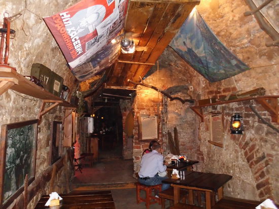 Genau gegenüber vom Rathaus kann man in einen Kellereingang eines Hauses gehen und, wenn man an der schweren Eisentür die richtige Partisanenlosung nennen kann, wird geöffnet und man wird mit einem Glas Wodka begrüßt. Hier führen Einheimische ihre Gäste hin. In den Kellergewölben eine große Kneipe, die einem unterirdischen Partisanenlager nachempfunden ist. Viele Dekorationsstücke wie MPs und Kriechgänge sind echt