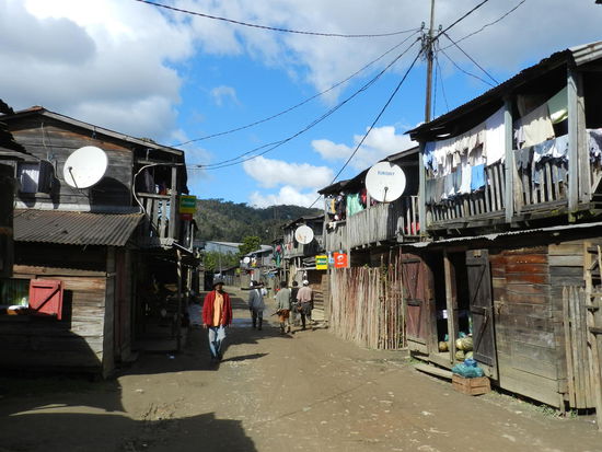 Ein armes Dorf, grobgezimmerte Holzhütten reihen sich die Hauptstraße entlang aneinander.