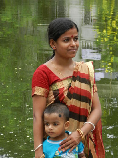 Mutter und Kind posen auf dem hinduistischen Opferfest am Tempelteich