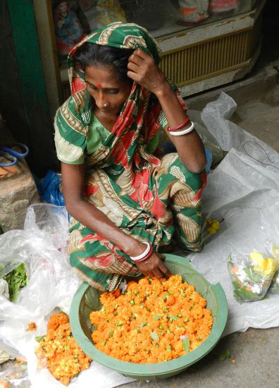 Sie verkauft vor einem Hindutempel Blütenschmuck
