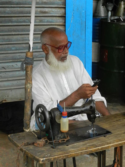 Ein Schneider sitzt vor seinem Laden im Hafen Dhakas