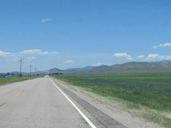 Meilenlange gerader Highway, gesäumt von grünen Wiesen und Feldern