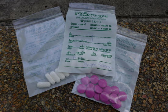 "Fuehlst du dich schlapp, geh zu Dr. Chusak!". Den Spruch kennen schon Kinder in ganz Thailand auswendig. Gesagt, getan! Wurde aber auch Zeit nach 4 Tagen ekliger Unpaesslichkeit am Stueck. Der Dorfdoktor von Kata kann sogar etwas Deutsch! Sein "Wartezimmer" besteht aus Plastikstuehlen und ist im Freien vor seinem Haus.
Herzig jedenfalls, wie hier die Pillen noch von Hand abgezaehlt, eingetuetet und die Tueten sogar teilweise auf Deutsch beschriftet werden! Insgesamt wurden nur laecherliche 20$ fuer die Konsultation inkl. Medikamente faellig!