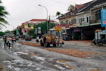Straßenbau kambodschanisch. Ein LKW kippt grobe Steinbrocken ins Loch, die Frauen klopfen sie mit dem Vorschlaghammer klein und die Walze macht dann alles platt. Mein Traumjob bei 32 °C und 98% Luftfeuchte