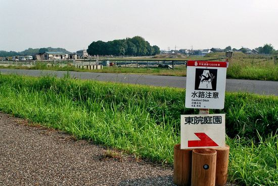 Dieser, ach so tiefe (20-30 cm), Graben war alle 20 m mit derartigen Warntafeln gesichert. Im Hintergrund Angestellte eier kleinen Baufirma beim Frühsport. (Nara)
