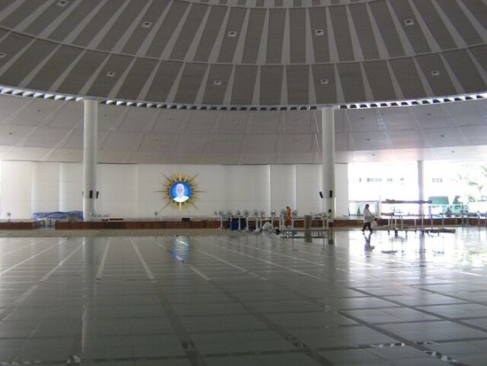 Die Vortragshalle, mit dem Bild des Sektengründers an der Wand. die Mönche sitzen auf den erhöhten Bereichen. Zur morgendlichen Speisung (Thai-Mönche nehmen nur eine Mahlzeit täglich, vor Sonnenhöchststand), kaufen Gläubige von der Kantine Speisen und legen sie in die Schalen.
Gerade die Art des Gründerkults und die bezahlte Speisung ist einer der Hauptkritikpunkte (auch meiner) an der Schule.