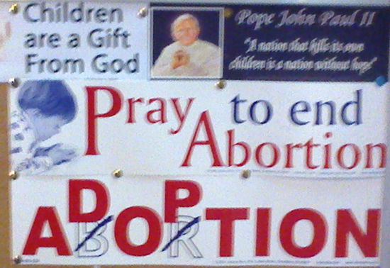 Feinste katholische Propaganda, ausnahmesweise einmal ein Schild in einer Fremdsprache. 
Am zweiten Tag unseres Aufenthalts parkten auf einem nahen Platz gut 20 LKW, um das Gepäck der Pilger für eine Massenwallfahrt zu transportieren. Sagen wir höchstens zwei Stück pro Mann, da war viel Platz. Vor der Antoniuskirche gab es den ganzen Tag Pilgerbüchlein. Um sechs Uhr am nächsten Morgen war die "kick off "-Messe dann auch überfüllt, auf den umliegenden Straßen entlang der Stadtmauer kein Stehplatz.