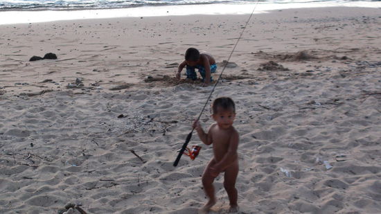 Wer klaut den da die Angel vom Papa. Kleiner hawaiianischer Bub am Strand.