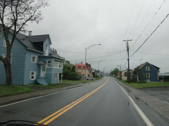 Ein kanadisches Dorf. So sehen fast alle Orte bei der Durchfahrt auf. Re. und li. Haus an Haus und vorne der gemähte Rasen. In der Mitte dann irgendwo die Kirche. Die gelbe Mittellinie darf man beim Abbiegen überfahren; aber Überholen ist beim Doppelstreifen verboten.