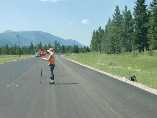 Auch Frauen sind beim Strassenbau tätig! Meist sind es ältere Frauen und Männer die sich per Funk mit dem Kollegen am anderen Ende der Baustelle verständigen und dann das Schild z.B. wie hier von 'Stop' auf 'Slow' drehen! Echt harte Arbeit bei diesen heißen Temperaturen die wir seit 2 Wochen aushalten mit regelmäßigen über 35 Grad!!!