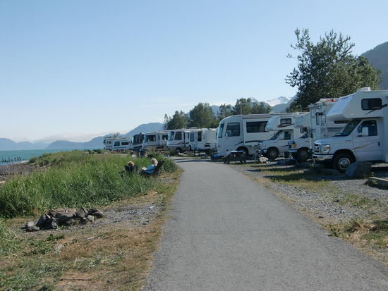 Camping an der Waterfront in Seward. Man kann die Bucht und die Berge aber nur von Fahrer- und Beifahrersitz aus sehen.
Der asphaltierte Weg ist für Radfahrer und Fußgänger gedacht; die Wohnmobilisten besetzen aber die Uferseite auch noch mit Tischen und Stühlen und grillen dort ab Spätnachmittag.
Ich bin noch etwas unschlüssig, aber eigentlich bin ich der Meinung, daß man die erste Linie hier für Womos sperren sollte und lieber die Promenade verbreitert, damit die Fußgänger das alles mehr genießen können. Denn an einer langen Reihe parkender Womos vorbei zu laufen ist nicht gerade so schön!