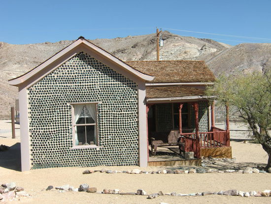 Geisterstadt Rhyolite: Das Bottle-House wurde aus 50.000 Whiskey- und Bierflaschen 1906 erbaut. Es ist aber offensichtlich inzwischen wieder bewohnt! Ein Zaun verhinderte das Näherkommen!
Die Stadt Rhyolite war einmal von 10.000 Einwohner bewohnt die wegen des Goldrausches hier ihr Glück suchten. Das dauerte nur 3 Jahre und 1916 verloschen die letzten Lichter in diesem Ort.
Heute besuchen einige Touristen diese verlassene Stätte in der es einmal sogar ein Opernhaus, mehrere Krankenhäuser und Banken und ein öffentliches Schwimmbad gegeben haben soll!
Meist sind hier nur Ruinen zu finden! Kaum etwas besser erhalten.