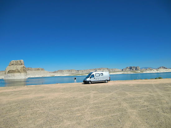Und dort standen wir dann!
Mit einem herrlichen Blick auf den Lone Rock auf dem Lone Rock CP
für 10$ die Nacht.
Lauwarme Außenduschen gab es auch bei den Washrooms.
Und Flush-Toiletten gab es sogar hinter uns am Strand.
Es gab auch noch viele weitere ganz hinten in den Dünen was mich schon etwas wunderte: Sind im Sommer so viele Leute hier?
Bis mir eine Deutsche erzählte daß der Wasserspiegel des Lake Powell seit Jahren erheblich sinkt und die Seefläche früher mal ganz oben war wo heute die Toiletten noch stehen!
Außerdem sieht man deutlich am Lone Rock wie hoch mal der Wasserspiegel jeweils war!