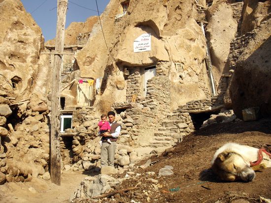 Vater mit Tochter vor den typischen hinkelsteinartigen Felsenhäusern Kandovans. Die Höhlenwohnungen sind in grauen Tuffstein gegraben, die einzelnen Tuffkegel sind mit Treppen verbunden.