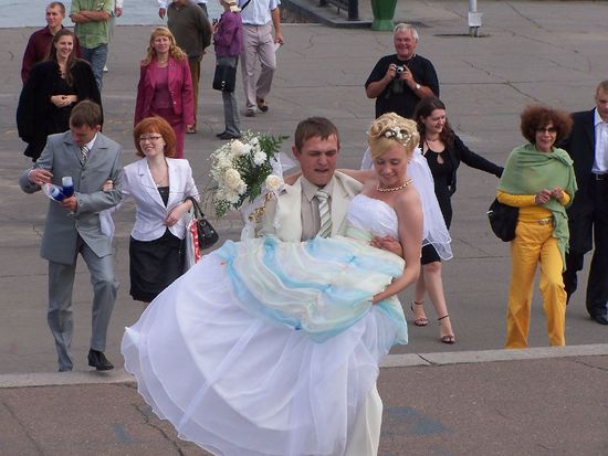 eher angestrengt als gluecklich traegt der Braeutigam seinen Braut ueber die Bruecke