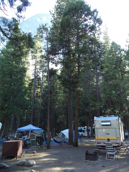 Wir stehen hier unter Bäumen und haben den Blick auf einen Felswand.