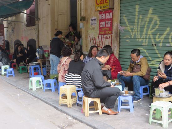Gäste in einem Straßenrestaurant auf kleinen Hockern