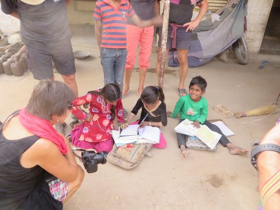 Die Kinder sitzen auf der Erde und machen Schulaufgaben, das kleine Mädchen schreibt mit sauberer Handschrift einen Text ab.