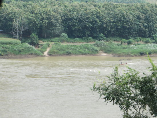 Auf dem Mekong fahren kleine Boote. Der Fluß ist gelb-braun und schmutzig.