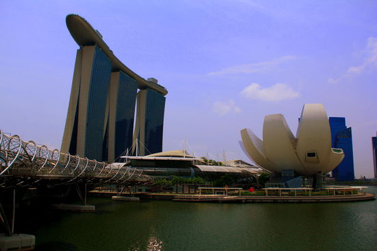 Links das Marina Bay Sands Hotel, welches 2010 eröffnet wurde. Die drei 55-stöckigen Hoteltürmen tragen auf 191 Meter Höhe einen 340 Meter langen Dachgarten. Das Resort gilt als die teuerste alleinstehende Kasinoanlage der Welt. Die Grundstückkosten eingerechnet, soll der Bau 8 Milliarden Singapur-Dollar (rund 4,6 Milliarden Euro) gekostet haben. 
Das weiße, blumig aussehende Gebäude ist das art science Museum.