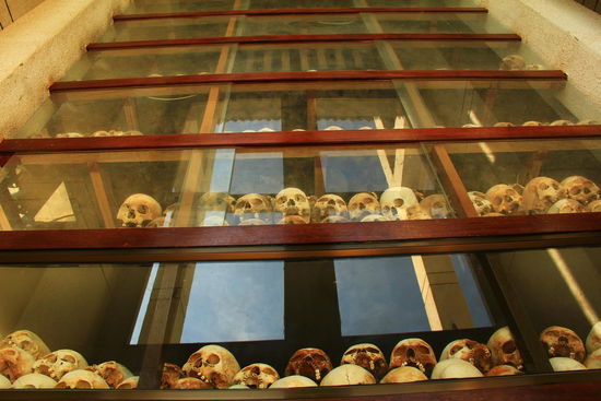 Die Schädel sind mit geschätzten Altersangaben der Opfer sowie der Todesursache markiert. Weiter oben sind Knochen, Kleider etc.