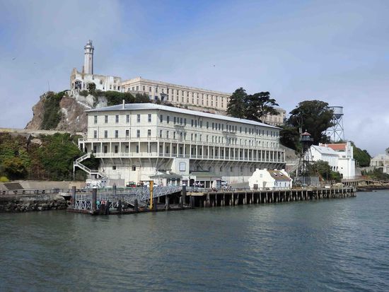 Im Vordergrund eines der Wohnhäuser und im Hintergrund der Zellentrakt mit dem Leuchtturm.