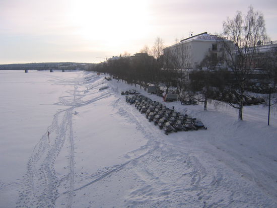 In Rovaniemi stehen am Ufer des (zugefrorenen und zugeschneiten) Flusses Kemijoki die Schneemobile bereit