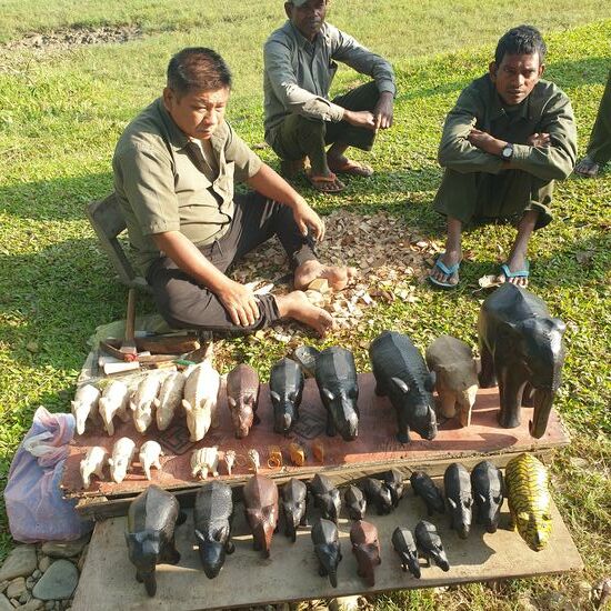 Bevor wir zu den Nashörnern aufgebrochen sind mussten wir nochmal zur Anlegestelle der Kanus. Bei einem Holzschnitzer hatte Ines am Vortag einen geschnitzten Tiger gesehen, den sie unbedingt noch einmal ansehen wollte. Die geschnitzten Nashörner und Elefanten sind alle sehr standardisiert. Bei den Tigern scheint es keine Vorlage zu geben und so sind sie recht individuell. Ines hat den Tiger im Rhinokörper dann gekauft. Im Bild rechts unten.