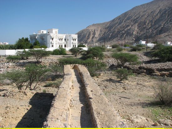 Am Ende des falaj ist eine Unterführung für das Wasser unter dem Wadi hindurch. das Gegenstück befindet sich an einem Baum vor dem weißen Haus. (Prinzip der kommunizierenden Röhren)