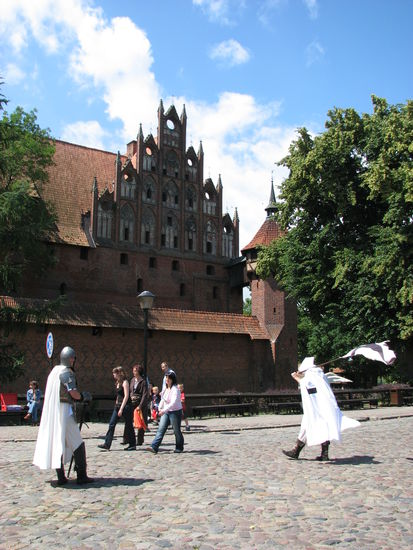 leider im Gegenlicht - aber die Fassade des hinter einem Graben befindlichen Eingangsgebäudes erinnert an die Verwandtschaft mit norddeutscher Backsteingotik. 
Touristische Auswirkungen in Form von "mittelalterlichen" Figuren bleiben auch nicht aus.