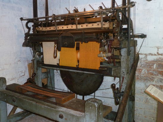 Handframe knitting machine
This example was developed from the first type of knitting machine, invented in 1589 by William Lee. It produced flat fabric, and was driven by the operator's hands and feet.
The machine knitting industry began by making stockings or "hose", the term "hosiery" became synonymous with the whole industry and is still used in this sense today. However, "hosiery", as applied to the industry's products refers only to stockings, tights and socks. The hosiery industry was the source of much of Leicester's prosperity for over two centuries.
Originally the machines were operated in homes or In small workshops. However by the mid 1800's changes in men's fashion had led to a decline in the handframe industry and many of the workers became employees in large mechanised hosiery factories, or left the Industry altogether to work In the newly emerging boot and shoe trade or the engineering industry.
By 1891 95per cent of knitted goods were produced in factories.
(Beschriftung an der Maschine)