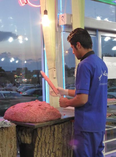 das gewürzte Gehackte wird in einer rasenden Geschwindigkeit auf breite Metallspieße aufgebracht und liegt dann neben Gemüsespießen für den Grillmeister bereit