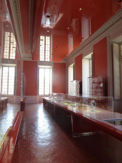 Stuckdecken mit abgehangenen Plastikdecken - Porzellan in Acrylglaszylindern/ -quadern  mit facettierten Glasplatten, die ein gebrochenes Licht auf die Gegenstände werfen.