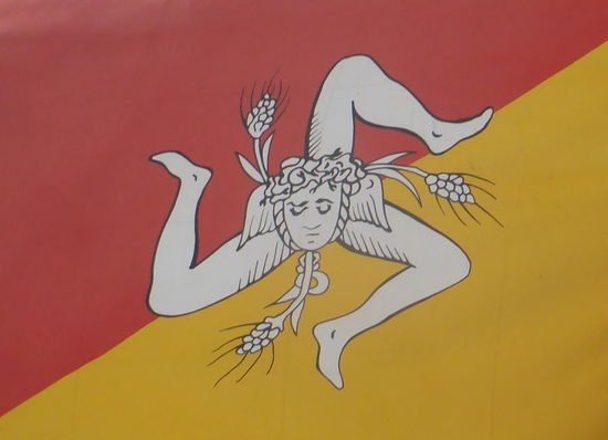 Die Flagge Siziliens existiert seit der Sizilianischen Vesper im Jahr 1282, als sich Sizilien gegen die Herrschaft Karls I. von Anjou auflehnte.
Der Hintergrund ist diagonal in rot und gelb unterteilt. In der Mitte wird eine Triskele mit einem verzierten Kopf dargestellt. (wikipedia)
Im Februar 2000 wurde die Flagge zur offiziellen Regionalflagge erklärt, die Sizilien vor allen öffentlichen Gebäuden repräsentiert.