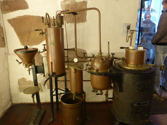 Dampfdestillationsapparat Fa. W. Schwarzenau, Berlin, um 1890
Die Industrialisierung hielt in den letzten Jahrzehnten des 19. Jh. auch in den Apotheken Einzug, verschiedenste neue Apparaturen erleichterten die Arbeit und ermöglichten größere Herstellungsmengen. Mittels des kohlebefeuerten Ofens dieser damals hochmodernen Apparatur konnte die Dampfdestiilation in der Apotheke wesentlich effektiver gestaltet und daneben mit jeweils einem Einsatz aus Porzellan und einem aus Metall Aufgüsse (Infuse) und Abkochungen (Dekokte) zubereitet werden.