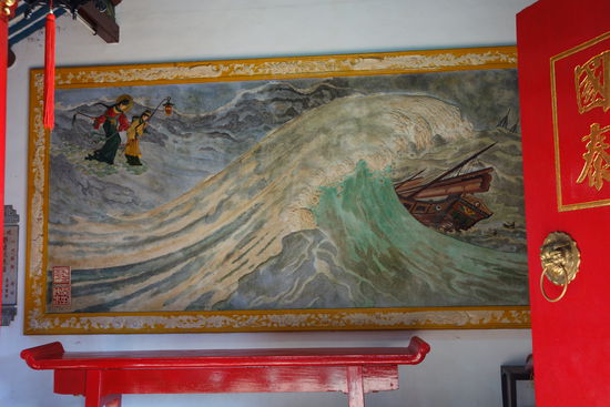 Das Wandbild am Eingang zeigt die Göttin Thien Hau bei dramtischem Wellengang schützend über einer Dschunke schweben