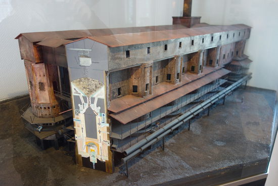 Messeler Schwelöfen
Die Schwelerei bildet das Zentrum der Messeler Ölschieferaufbereitung. Die trockene Destillation des Ölschiefers erfolgt in diesen speziell entwickelten Öfen, wobei die Beheizung von innen erfolgt. In einem kontinuierlichen Ablauf konnten die einzelnen Schwelschritte durchgeführt werden. Insgesamt waren 32 Rundöfen erbaut worden von denen jeder einen Tagesdurchsatz von 26 Tonnen Ölschiefer hatte. Im Innern jedes Rundofens waren 24 Retorten kreisförmig angeordnet. Im Gegenstromprinzip wurden diese durch die Heizgase erwärmt. Somit war eine exakte Temperaturführung möglich. Im oberen Bereich erfolgte bei ca. 120°C die Trocknung des Ölschiefers. In der darunter folgenden Vergasungszone erfolgte die Bildung des Rohöls bei ca. 500°C Das Rohöl wurde abgeführt und in der Kondensation abgekühlt und in flüssige Form überführt. In der untersten Zone, dem »Krätzeraum« fielen die Rückstande bei einer Temperatur von ca. 1200°C alle 40 Minuten an. Diese wurden mit einem Elektroschieber aus den Öfen abgezogen und teilweise  weiter verarbeitet.