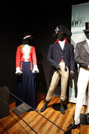 Frauenkleidung - um 1789, Mode während der Französischen Revolution
Jacke (Caraco) und Rock, in den französischen Nationalfarben bJau-weiß-rot, darunter eine Bluse, Unterrock und Gesäßpolster darüber eine Taillenschärpe, Schlupfschuhe und Hut mit Bandrosette
Herrenkleidung - um 1789, Mode während der Französischen Revolution
dunkelblauer Tuchrock mit Napoleon-Kragen, Hose mit angedeuteten Hosenträgern, Hemd, rote Weste, Zweispitz-Hut mit blau-weiß-roter Concarde und kurzen StiefeIn