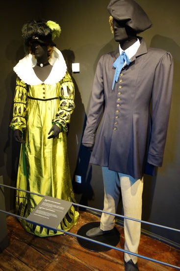 Männerkleidung „Teutsche Nationaltracht" - um 1815
Hemd mit abgenähten Biesen und blauer Schleife, darüber ein schlichter Leibrock, lange Hose, Knöchelschuhe, auf dem Kopf ein sogenanntes Wagner-Barett
Frauenkleidung „Teutsche Nationaltracht" - um 1815
enger Unterrock, darüber ein Kleid mit hoch stehendem Spitzenkragen und Puffärmeln mit Schlitzen, Samthalsband, auf dem Kopf ein Hut mit Federschmuck
Studenten und Künstler trugen diese Mode