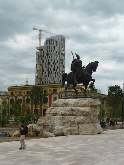 Skanderbeg-Denkmal - mit unfertiger 'Bausünde' dahinter - das rot-gelbe Gebäude in italienischem Stil beherbergt Ministerien